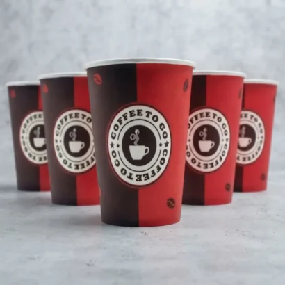 Red and black cardboard coffee cups on a dark surface with coffee beans